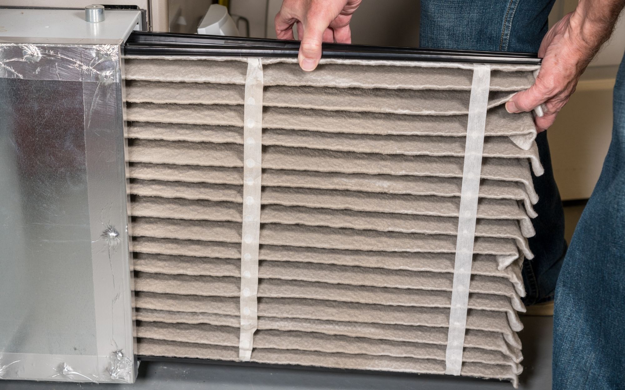 A dusty old musty air filter is being pulled out of the HVAC system