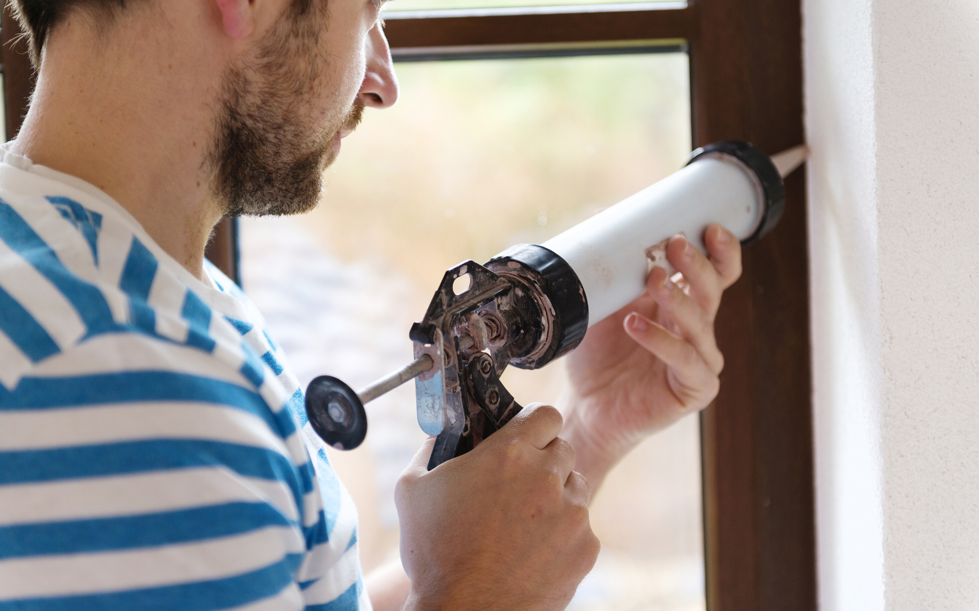 Man Using a Caulking Gun to fill crack by window