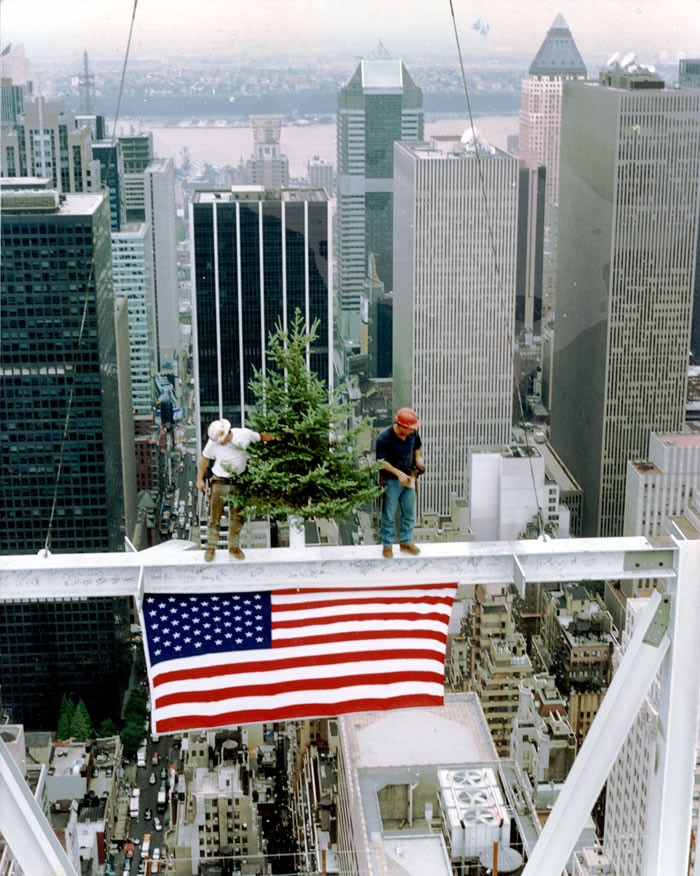 Mohawk iron workers stand witha pine tree on a steel beam above New York city with an American flag hanging from the beam