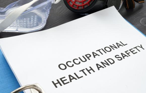 An image of a binder on a table open to a title page that says "Occupational Health and Safety" with safety goggles on the table next to it