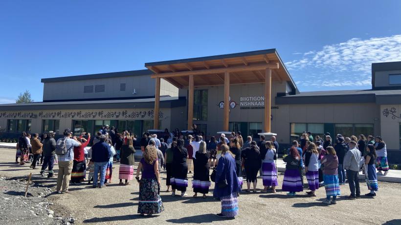 community members stand outside of the new school, facing the school and away from the camera, observing the beautiful new building