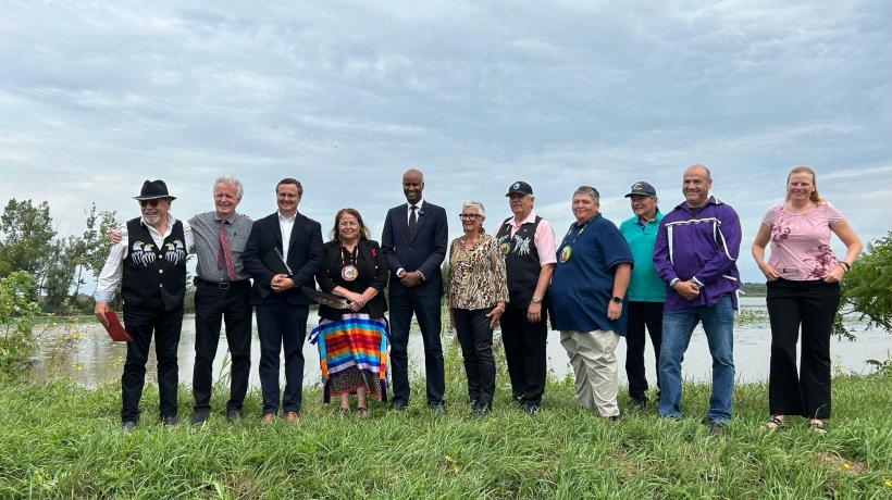 a group of officials stand together in front of a body of water.